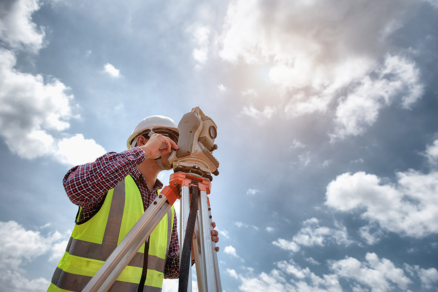Land Surveyor Insurance - Worker Looking Over Land to Survey with a Bright Blue Sky